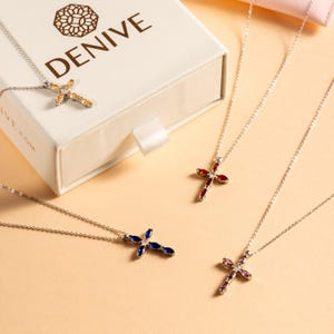 May include: Four silver necklaces with cross pendants featuring different colored gemstones. The crosses are adorned with clear and colored gemstones, including yellow, red, blue, and purple.