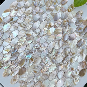 May include: A mosaic tile design featuring numerous iridescent, oval-shaped pieces in shades of white, cream, and brown. The tiles are arranged in a repeating pattern, creating a textured surface. The mosaic is set on a white square.