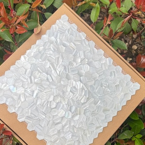 Puede incluir: Una taza de cerámica blanca con un asa negra y el texto "But First, Coffee" en negrita negra. La taza está sobre una superficie blanca. La taza mide aproximadamente 10 cm de alto.