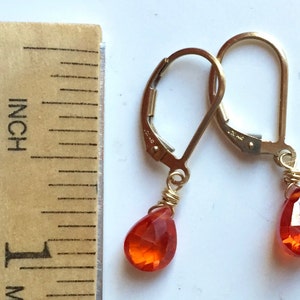 May include: Gold-tone leverback earrings with teardrop-shaped, faceted orange gemstones. The earrings are approximately 0.5 inches in length, as measured by a wooden ruler. The gemstones are wire-wrapped to the earring hooks.