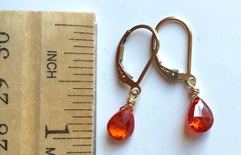 May include: Gold-tone leverback earrings with teardrop-shaped, faceted orange gemstones. The earrings are approximately 0.5 inches in length, as measured by a wooden ruler. The gemstones are wire-wrapped to the earring hooks.