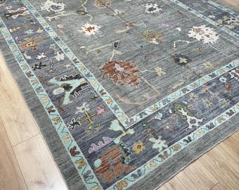 May include: A large, rectangular area rug with a gray background and a detailed floral pattern in shades of brown, yellow, and blue. The rug has a border with a repeating design and a light blue trim.