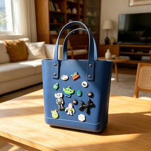 May include: A navy blue tote bag with two handles and decorative pins. The bag is adorned with colorful cartoon character pins, including an alien, a robot, and a dog-shaped balloon. The bag is sitting on a wooden table.