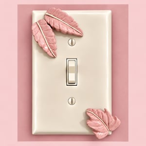 Op de afbeelding: Een rechthoekige gebroken witte lichtschakelaarplaat met driedimensionale roze keramische bladeren op het oppervlak. De plaat bevat een centrale tuimelschakelaar en twee zilveren schroeven voor montage, met twee bladeren linksboven en één rechtsonder.