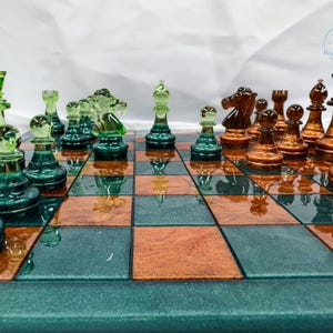 May include: A chess set featuring a board with alternating dark green and copper-colored squares. The pieces are made of translucent glass, with one set in a vibrant green hue and the other in a deep amber brown, arranged in a game setup.