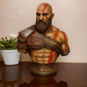 Puede incluir: Busto detallado de un guerrero calvo y barbudo con marcas rojas en la cabeza y el cuerpo. Viste una armadura de cuero marrón con diseños intrincados. El busto está sobre una base decorativa, mostrando una expresión severa.