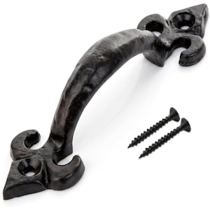 May include: A black metal door handle with a textured, hammered finish and a fleur-de-lis design at each end. The handle features two mounting holes at the base of each decorative end and is accompanied by two matching black metal screws.