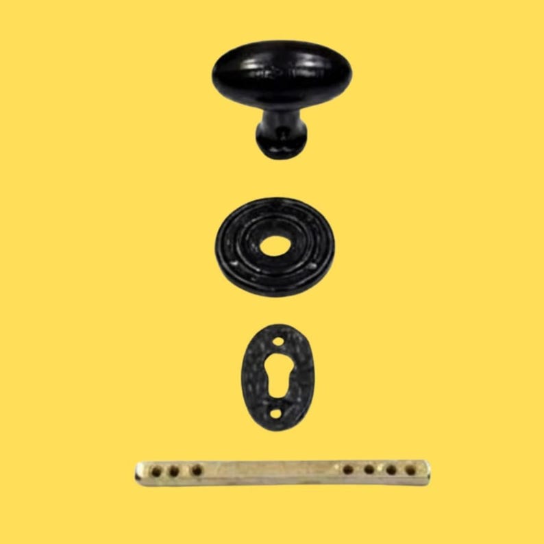 Puede incluir: Un pomo de puerta ovalado negro, un roset&oacute;n circular negro, una placa de cerradura ovalada negra y un eje met&aacute;lico rectangular con varios orificios. Estos componentes de herraje est&aacute;n dispuestos verticalmente sobre un fondo amarillo.