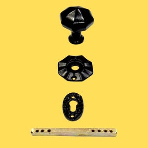 Puede incluir: Un pomo de puerta negro de forma octogonal, una placa octogonal negra a juego, un escudo de cerradura ovalado negro y un eje met&aacute;lico rectangular con varios orificios, todo sobre un fondo de color amarillo s&oacute;lido.