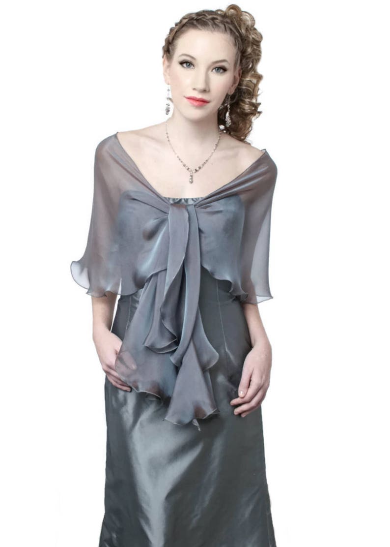 May include: A grey sheer shawl with a ruffled trim and a bow at the neck. The shawl is made of a lightweight fabric and is perfect for adding a touch of elegance to any outfit.