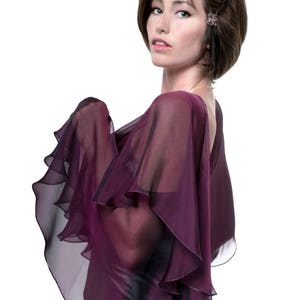 May include: A woman wearing a purple, sheer, ruffled shawl. The shawl has a layered, cascading design.