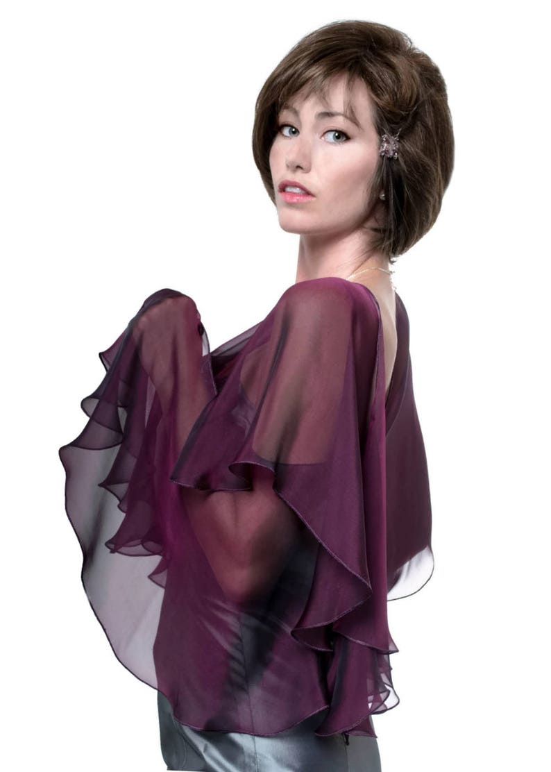 May include: A woman wearing a purple, sheer, ruffled shawl. The shawl has a layered, cascading design.