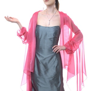 May include: A woman wearing a gray strapless dress with a pink chiffon shawl. She is wearing a pearl necklace and earrings.