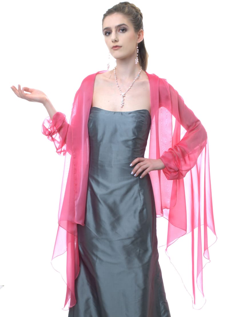 May include: A woman wearing a gray strapless dress with a pink chiffon shawl. She is wearing a pearl necklace and earrings.