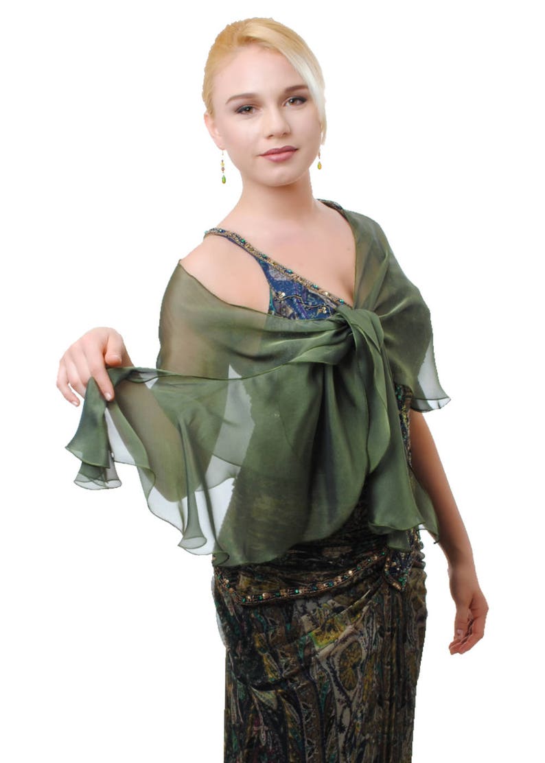 May include: A woman wearing a green chiffon shawl over a patterned dress. The shawl is tied at the neck and has a ruffled edge.