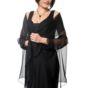 May include: A woman wearing a black dress with a sheer black shawl. She is wearing a black beaded necklace with a gold pendant.