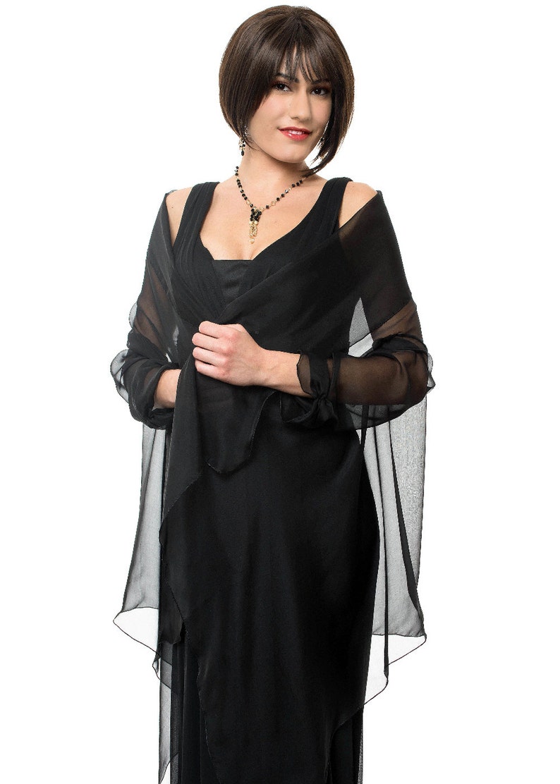 May include: A woman wearing a black dress with a sheer black shawl. She is wearing a black beaded necklace with a gold pendant.