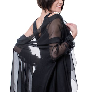 May include: A woman wearing a black dress with a sheer black shawl draped over her shoulders. She has short dark hair and is looking over her shoulder.