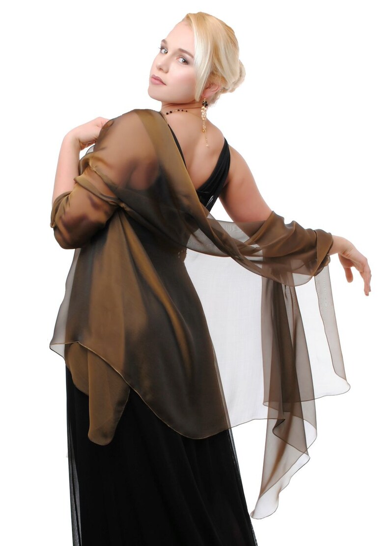 May include: A woman wearing a black dress with a brown sheer shawl draped over her shoulders. She is looking over her shoulder with a slight smile.