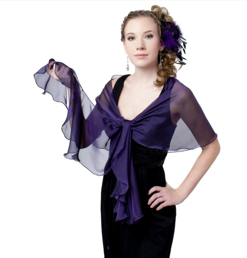 May include: A purple chiffon shawl with ruffled edges. The shawl is draped over the shoulders of a person wearing a black dress.