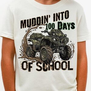 May include: A white t-shirt with a graphic of an ATV and the text "Muddin' Into 100 Days of School". The ATV is brown and green, with mud splatters around it. The text is in black and green.