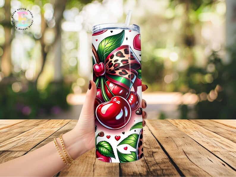 Puede incluir: Un vaso blanco con un dise&ntilde;o de cerezas. El dise&ntilde;o incluye cerezas rojas, hojas verdes, un lazo con estampado de leopardo y peque&ntilde;os corazones. El vaso tiene una tapa plateada y una pajita blanca.