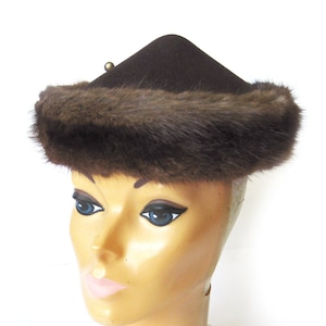 May include: A brown felt hat with a brown fur trim. The hat has a pointed crown and a wide brim. The hat is sitting on a white mannequin head.