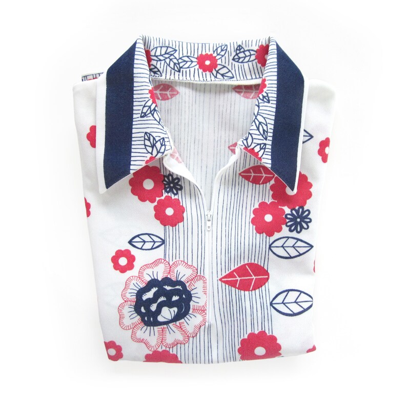 May include: A white collared shirt with a blue trim and a zipper closure. The shirt has a floral pattern with red and blue flowers and leaves.