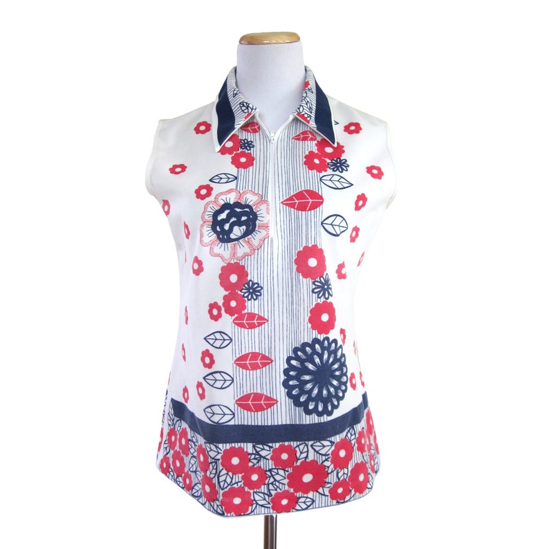 May include: A sleeveless white shirt with a blue and white striped collar and a zipper closure. The shirt has a red and blue floral pattern.