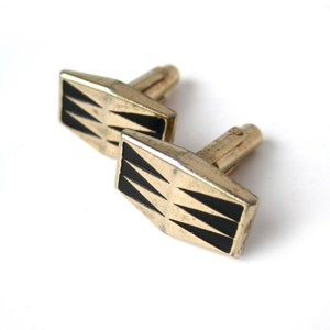 May include: A pair of gold cufflinks with black triangular designs.