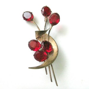 May include: A vintage brooch with a gold-toned metal base and a design of red glass stones arranged in a floral pattern.
