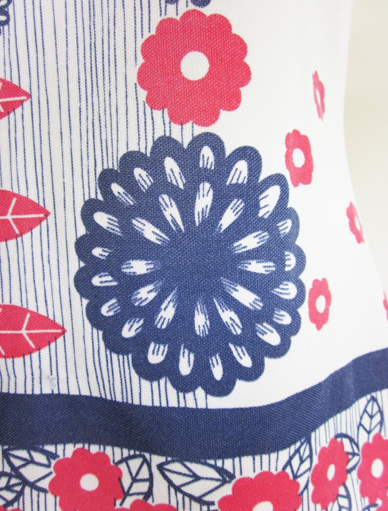 May include: White fabric with a blue and red floral pattern. The fabric features a large blue flower with white petals and a smaller red flower with a white center.
