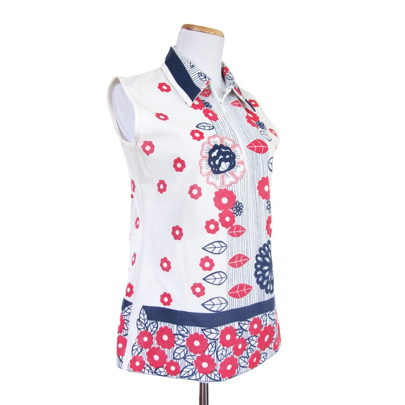 May include: A white sleeveless shirt with a blue collar and a floral print in shades of red and blue. The shirt has a blue and white striped pattern on the front and a floral pattern on the bottom.