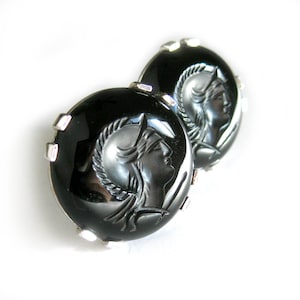 Op de afbeelding: Een paar zwarte onyx oorbellen met zilveren instellingen. Elke oorbel heeft een cameo van een vrouwenprofiel met een helm.