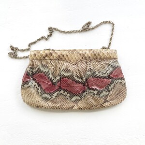 Peut inclure: Une pochette vintage avec une chaîne argentée. Le sac présente un motif peau de serpent dans les tons beige, marron et rouge. Le rabat supérieur a un design pointu unique.