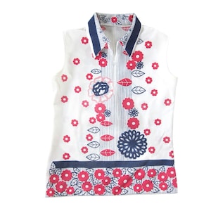 May include: A sleeveless white collared shirt with a blue and white striped collar and a zipper closure. The shirt has a floral pattern with pink and blue flowers and leaves.