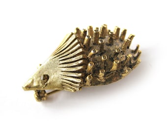 May include: A gold-toned brooch in the shape of a hedgehog. The hedgehog has a detailed, textured body and a spiky back.