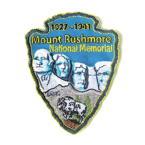 May include: A blue and yellow embroidered patch with the text "Mount Rushmore National Memorial" and the dates "1927-1941". The patch features an image of the four presidents carved into the mountain.