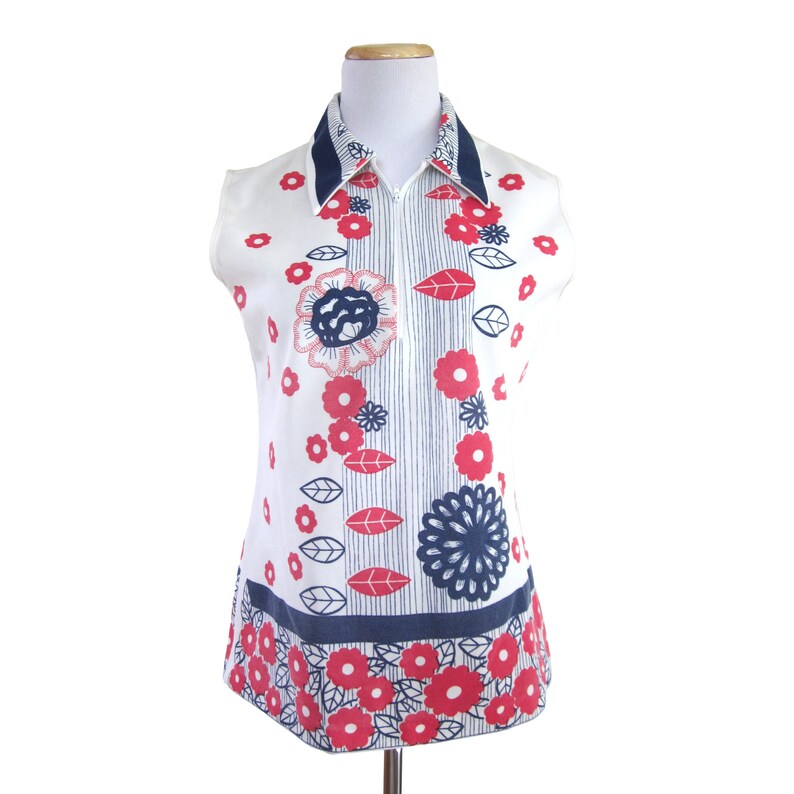 May include: A sleeveless white blouse with a blue collar and a zipper closure. The blouse features a red and blue floral print.