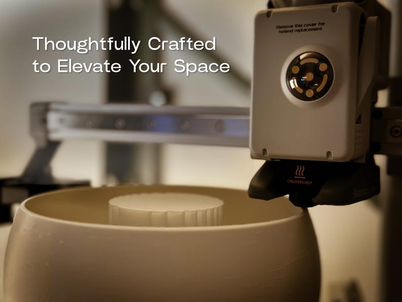 May include: A 3D printer with a white bowl and a white cylindrical object inside. The printer has a black nozzle and a white control panel with the text "Thoughtfully Crafted to Elevate Your Space".