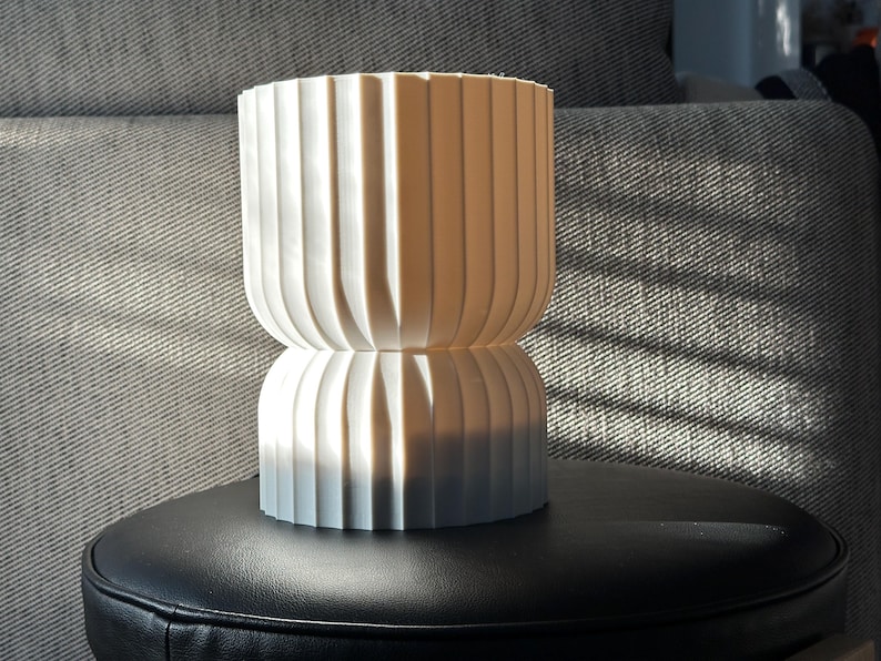 Modern table lamp, turned off, positioned on a black leather stool. Natural light highlights the lamp’s sculptural qualities, creating interesting shadows and emphasizing its elegant design.