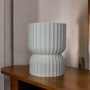 Modern table lamp, turned off, sitting on a wooden surface in a naturally sunlit room. Its minimalist design looks striking even when not illuminated, adding elegance and warmth to the inviting space.