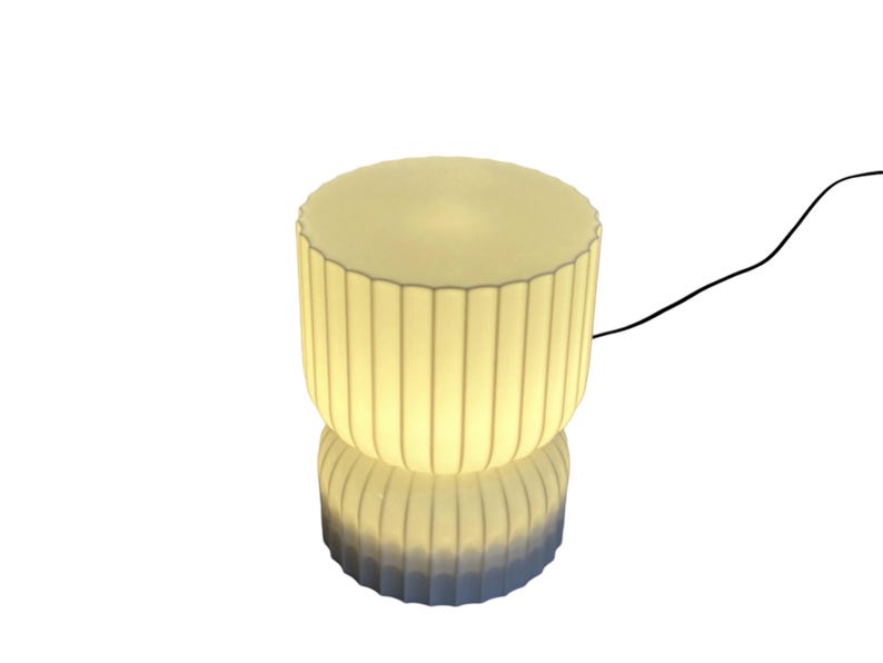 Full view of a modern table lamp, turned on, against a clean white background. Inspired by Japanese rice paper lamps, its minimalist design features soft lines, ready to emit a warm ambient glow when lit.
