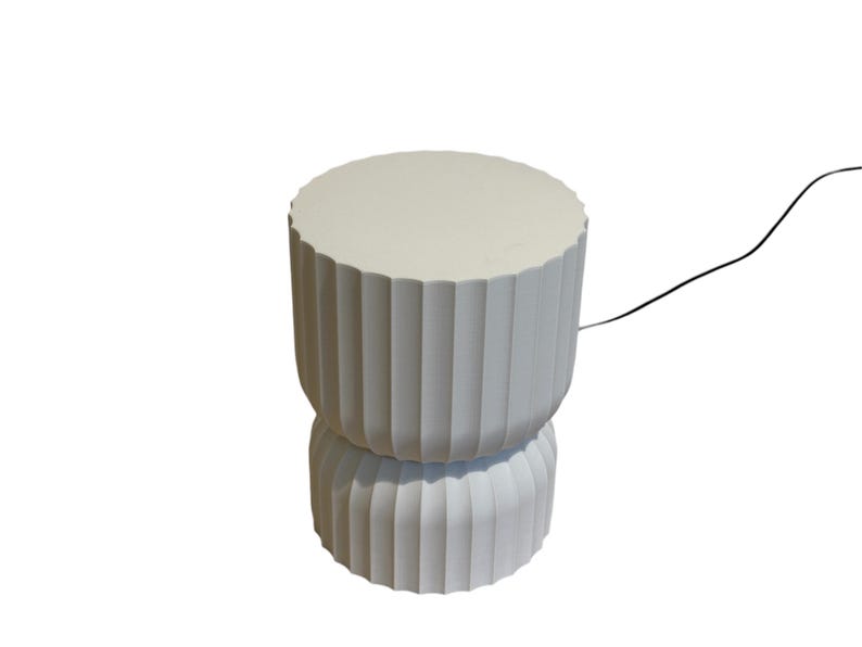 Full view of a modern table lamp, turned off, with a white background. Inspired by Japanese rice paper lamps, it emits a warm, diffused light, highlighting its minimalist design and soft ambient glow.