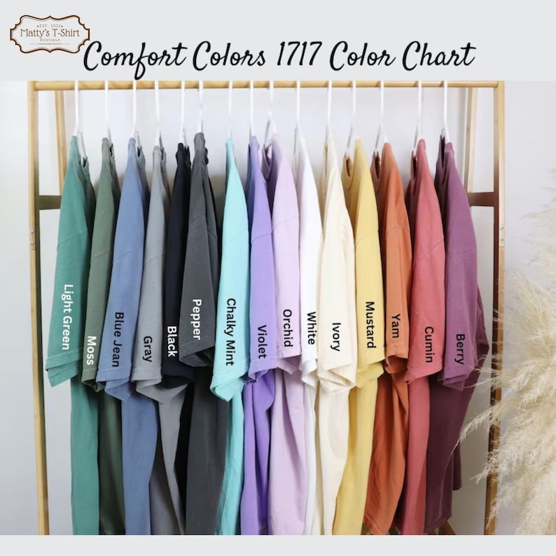 May include: Color chart showing 14 different colors of t-shirts hanging on a rack. The colors are: Light Green, Moss, Blue Jean, Gray, Black, Pepper, Chalky Mint, Violet, Orchid, White, Ivory, Mustard, Yam, Cumin, and Berry.