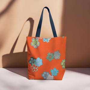 May include: Orange tote bag with a floral pattern featuring blue, green, and white flowers. The bag has navy blue handles.