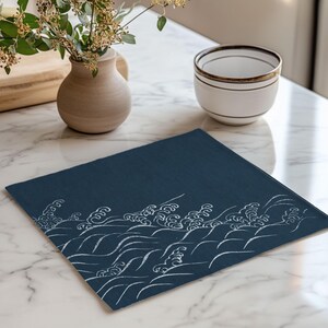 May include: A blue placemat with a white wave design. The placemat is made of a textured fabric and has a subtle sheen.