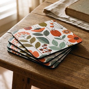 May include: A stack of four square coasters featuring a white background with a repeating botanical pattern of orange flowers, olive green leaves, and small red berries. The coasters have rounded corners and a thin black edge visible on the sides.
