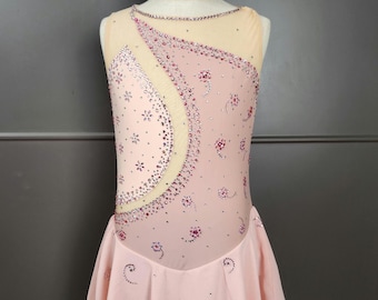 May include: A light pink figure skating dress with a sheer neckline and a flowing skirt. The bodice is embellished with rhinestones and floral designs. The dress is sleeveless and has a delicate, feminine appearance.