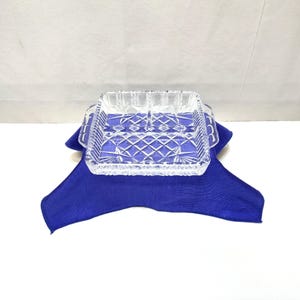 May include: A clear, square glass serving dish featuring a divided interior and a textured, diamond-cut pattern on the exterior. The dish includes two small handles on opposite sides and is constructed from transparent, pressed glass material.